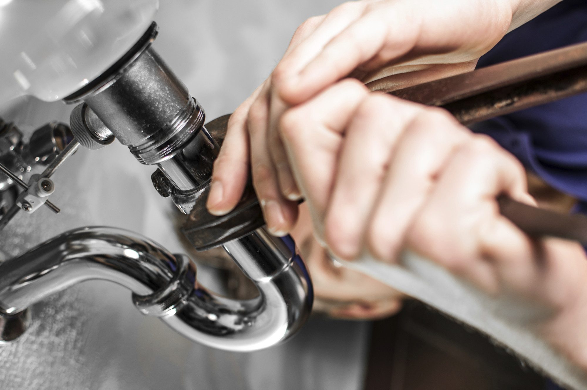 A plumber tightening a chrome basin trap with a wrench